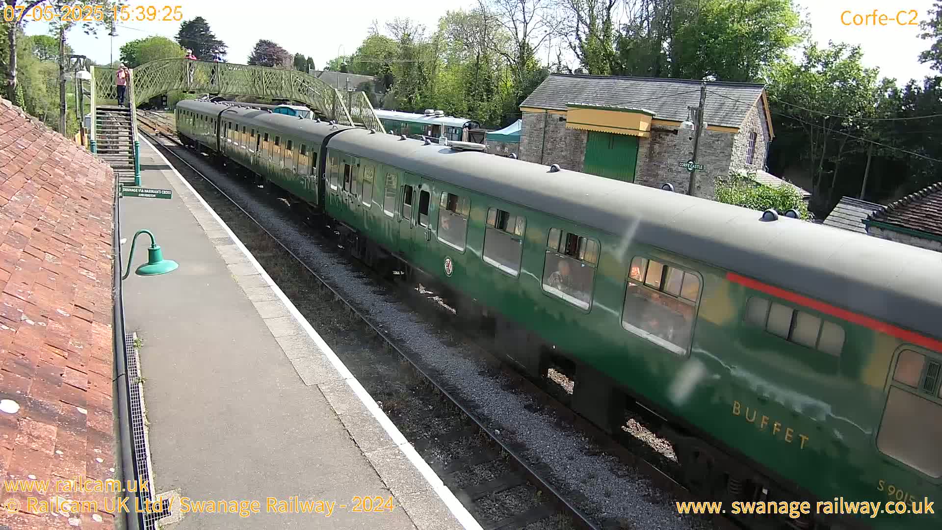 A long green passenger train departs a station on a sunny day.