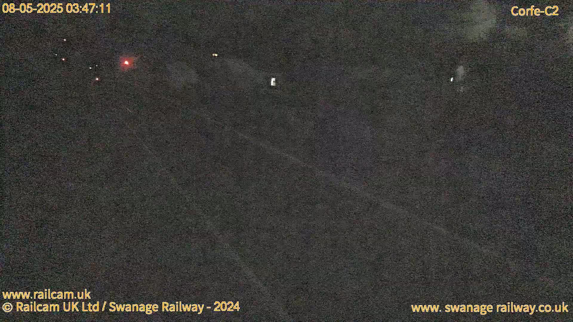 A dark, nighttime view of a roadway with a few faint lights visible in the distance.