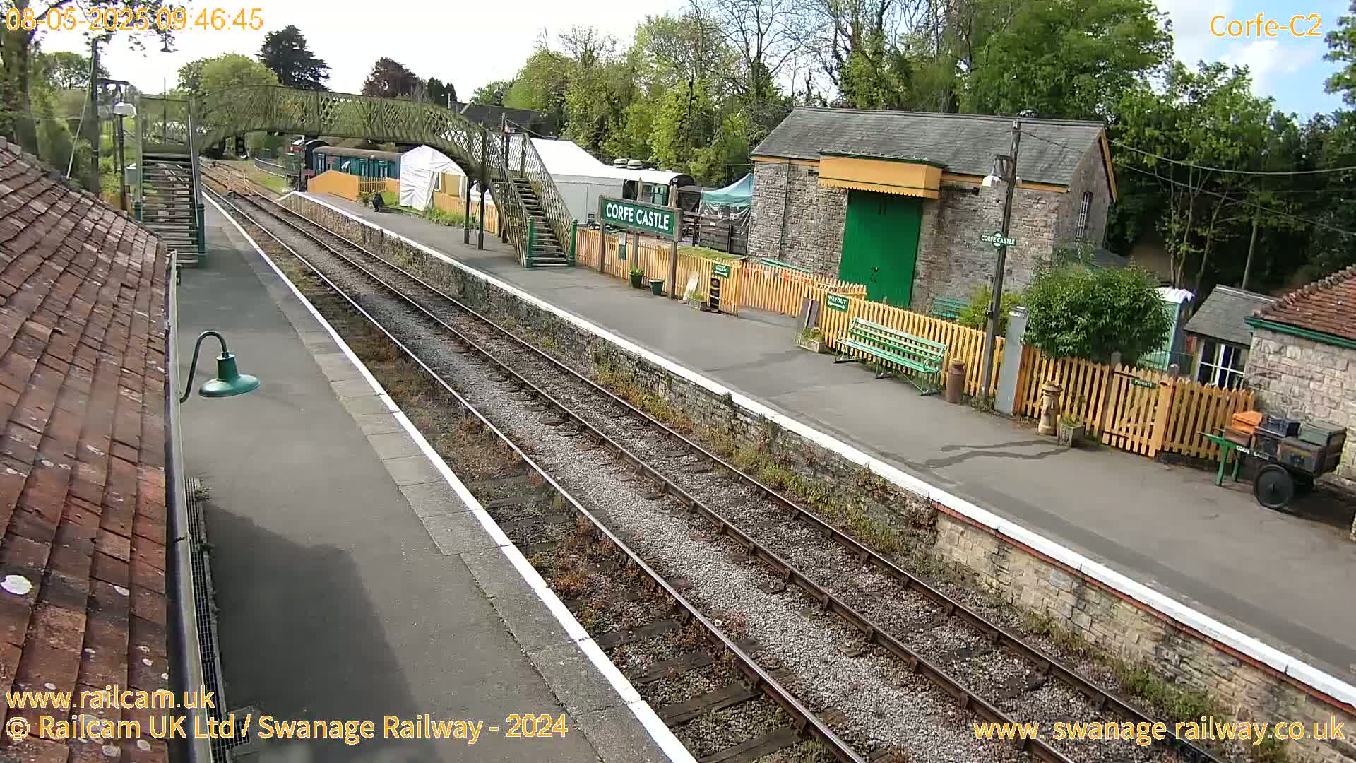 A train station platform with two train tracks under a partly sunny sky.