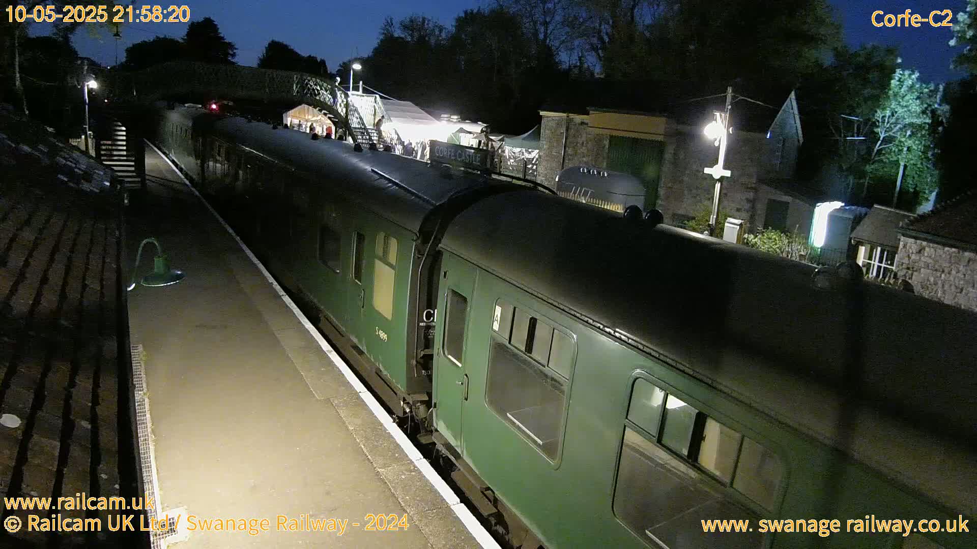 A dark green passenger train sits at a nighttime station platform under a dark sky.