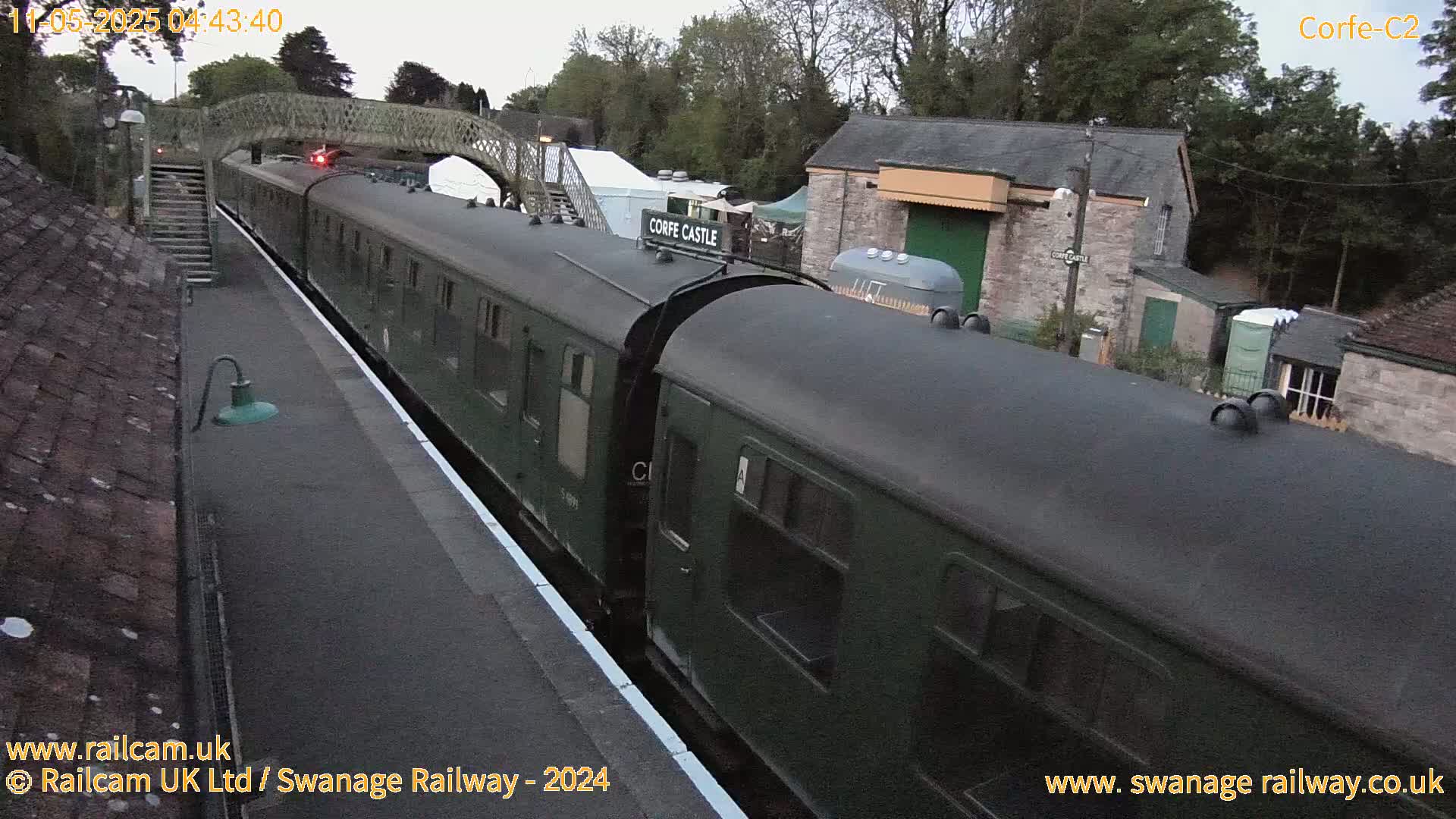 A dark green passenger train sits at a station on an overcast day.
