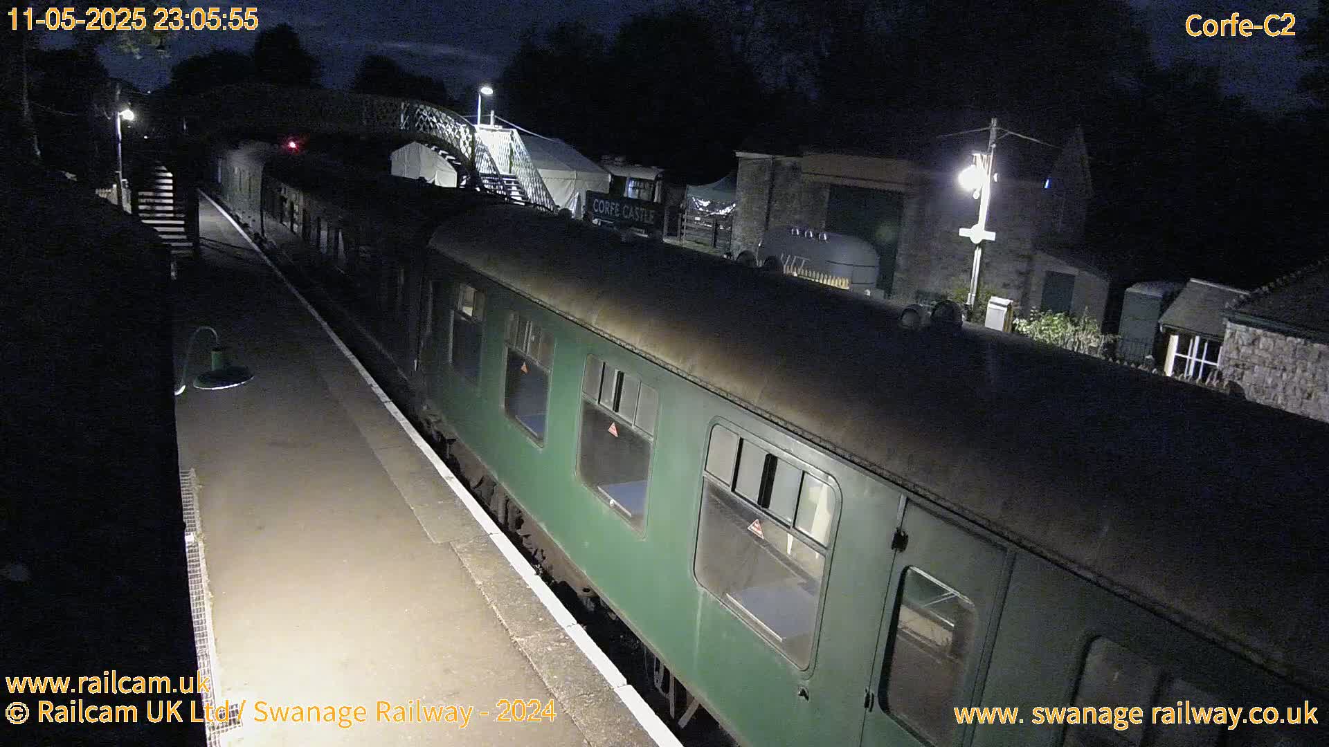 A dark green passenger train sits at a nighttime railway station platform under a mostly clear night sky.