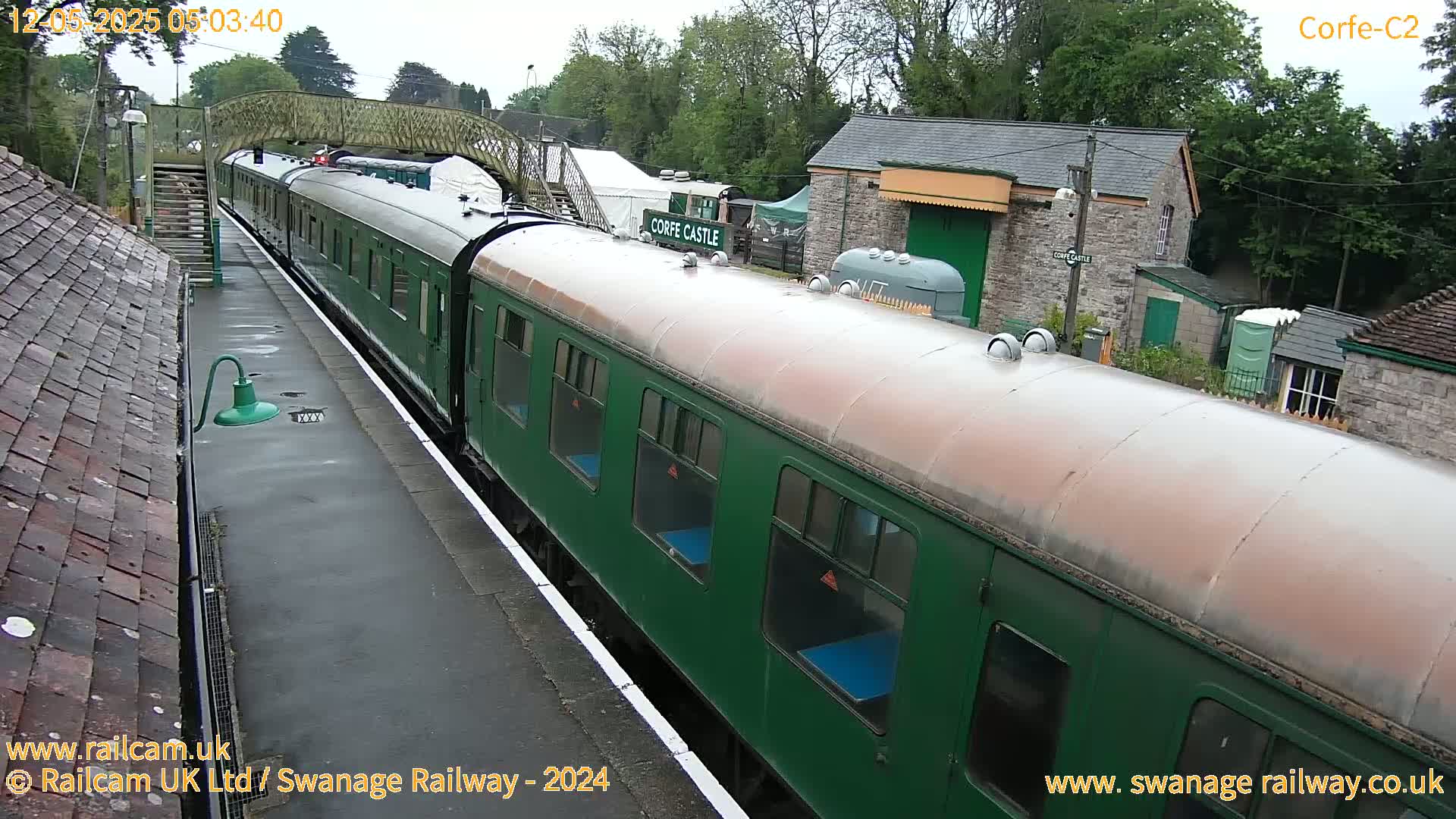 A dark green passenger train sits at a station on an overcast day.