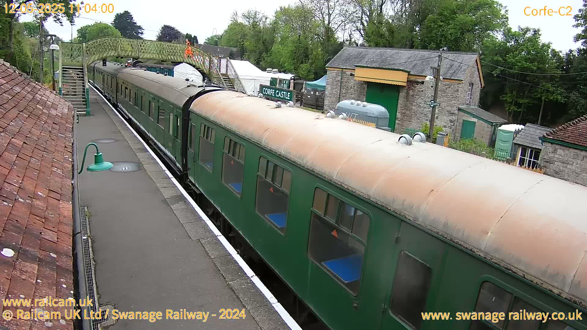 A long, dark-green passenger train sits at a station platform on an overcast day.