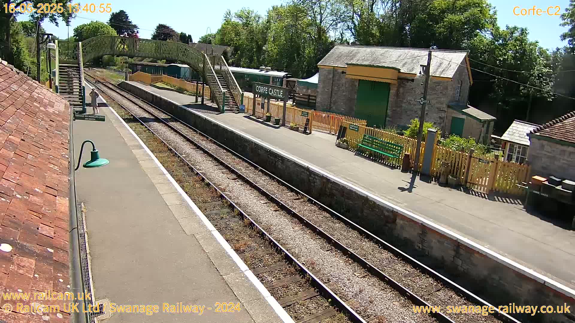 A sunny day at a train station with two parallel train tracks, a platform, a small building, and a footbridge.