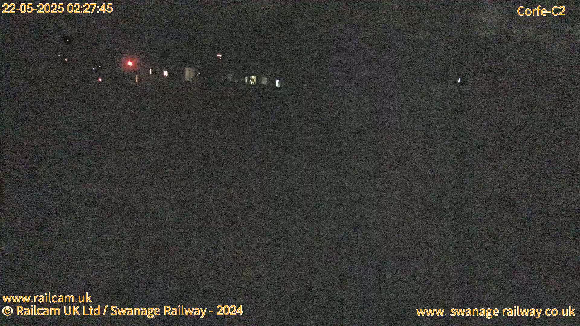 A nighttime, low-light view of a dark landscape with a few faint lights visible in the distance.