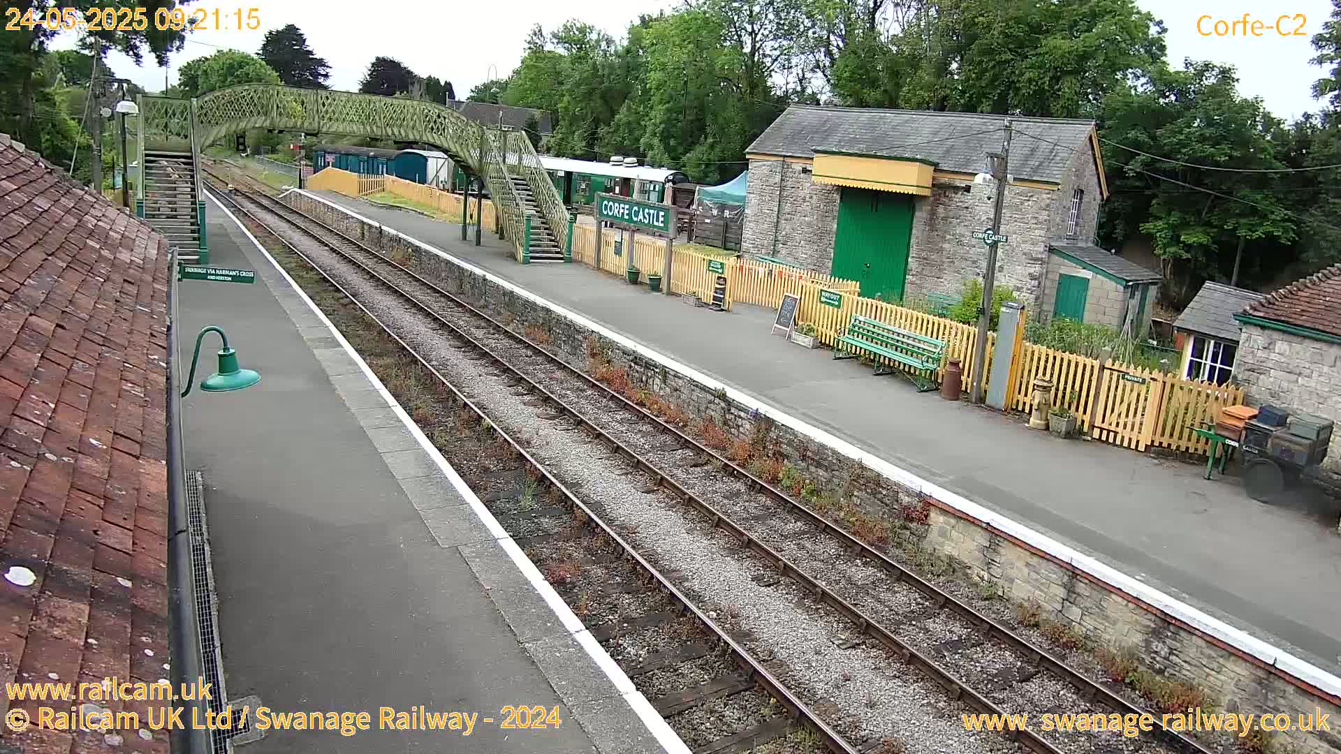 A train station platform with a railway line, a covered walkway, and stone buildings under an overcast sky.
