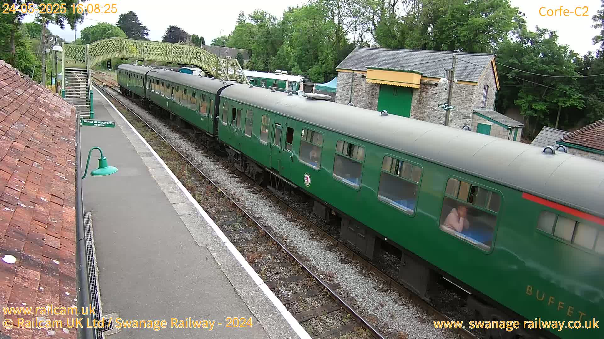 A long green passenger train is at a station on an overcast day.