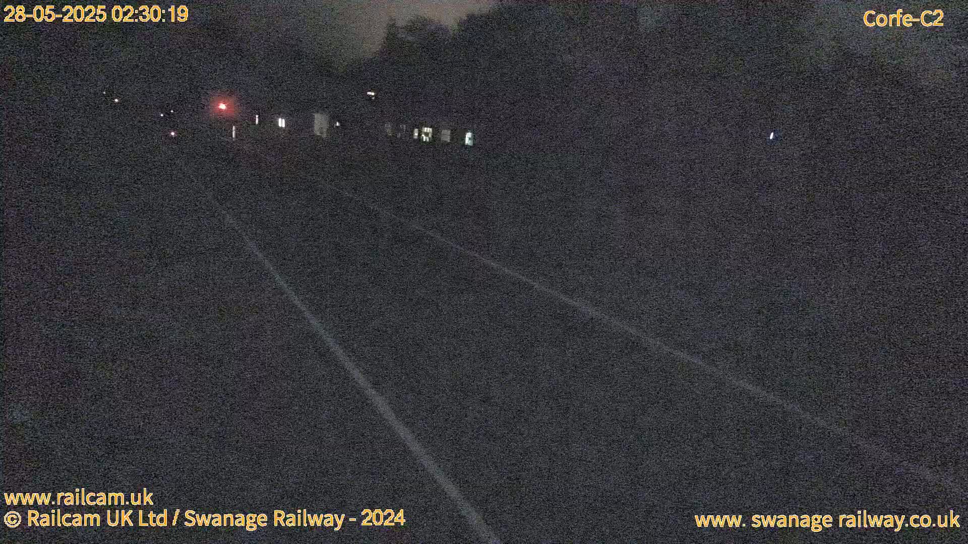A dark, nighttime view of a railway track with faint white lines marking the edges.