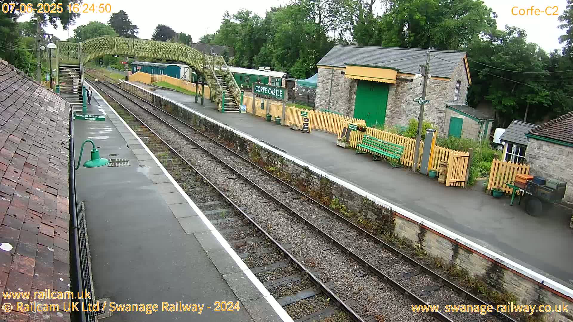 A train station platform with two train tracks, a railway car, and several stone buildings is viewed on an overcast day.