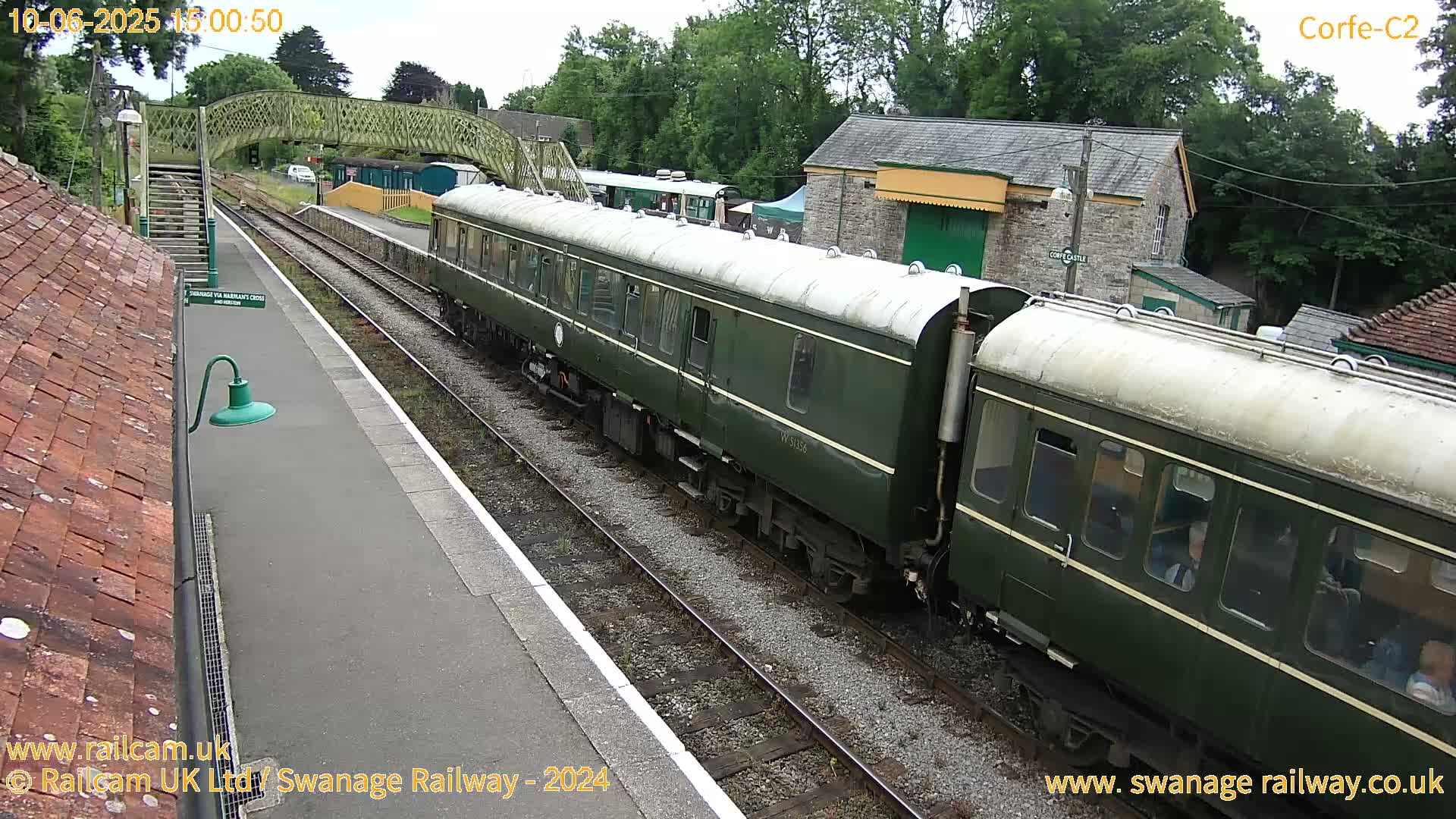 A dark-green passenger train sits at a station on a partly cloudy day.