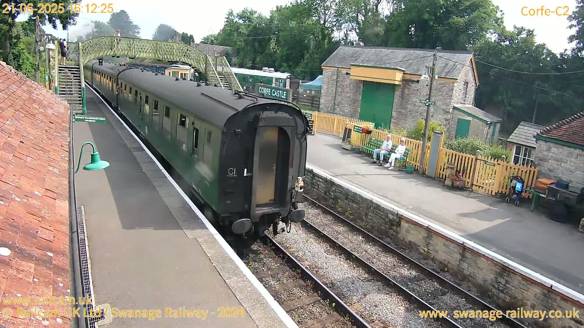A green passenger train departs a station on a sunny day.