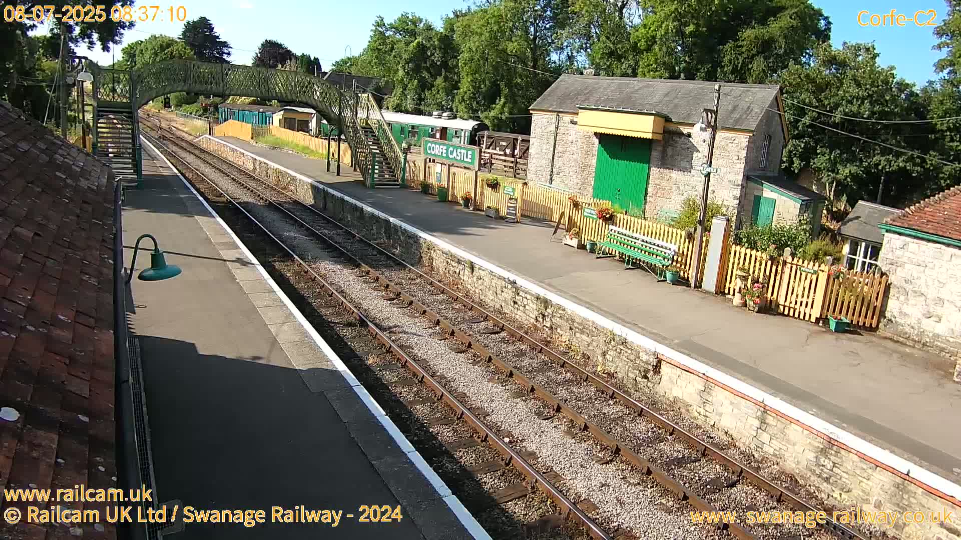 A sunny day at a train station with a railway platform, tracks, and stone buildings.
