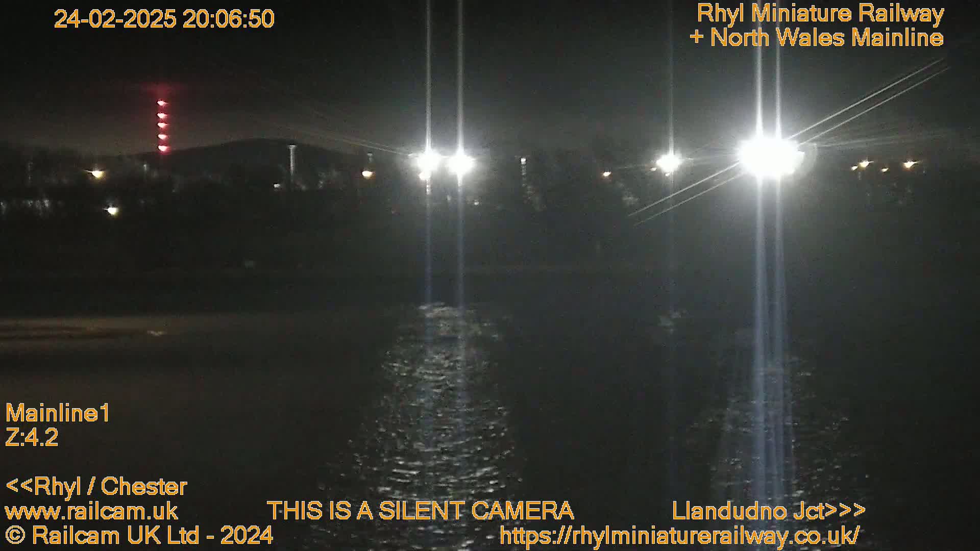 A nighttime view of a dark body of water reflecting bright lights from a nearby structure, under a clear sky.