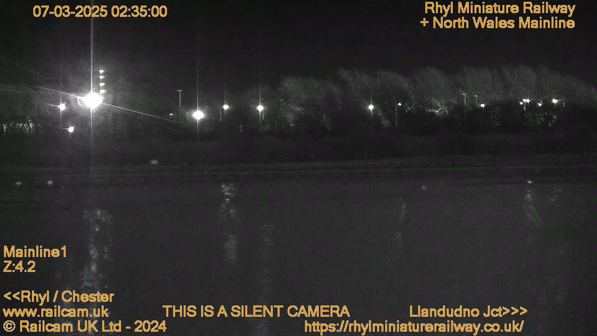 A nighttime view of a dark body of water reflecting lights from a tree-lined shore.