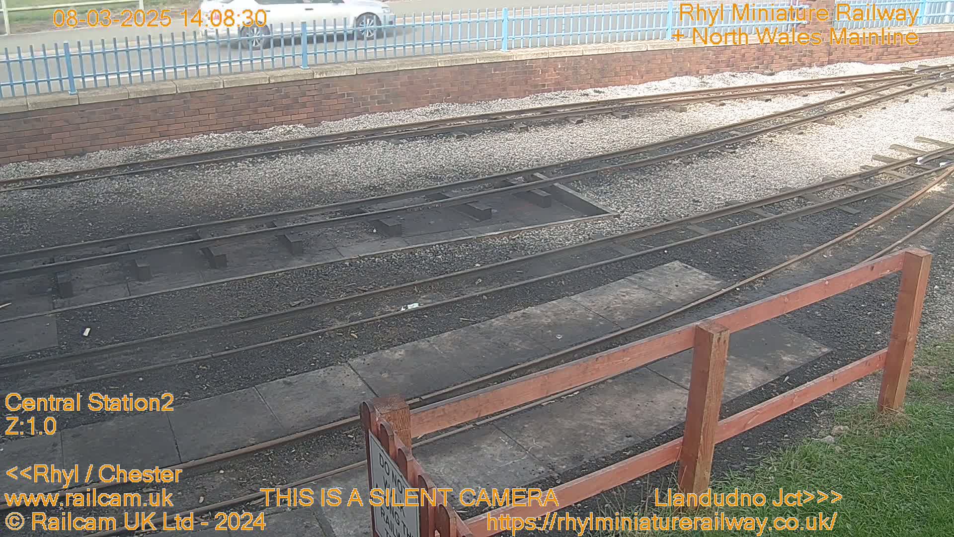 A section of railway track with a wooden fence and gravel ballast, viewed from above on a seemingly overcast day.