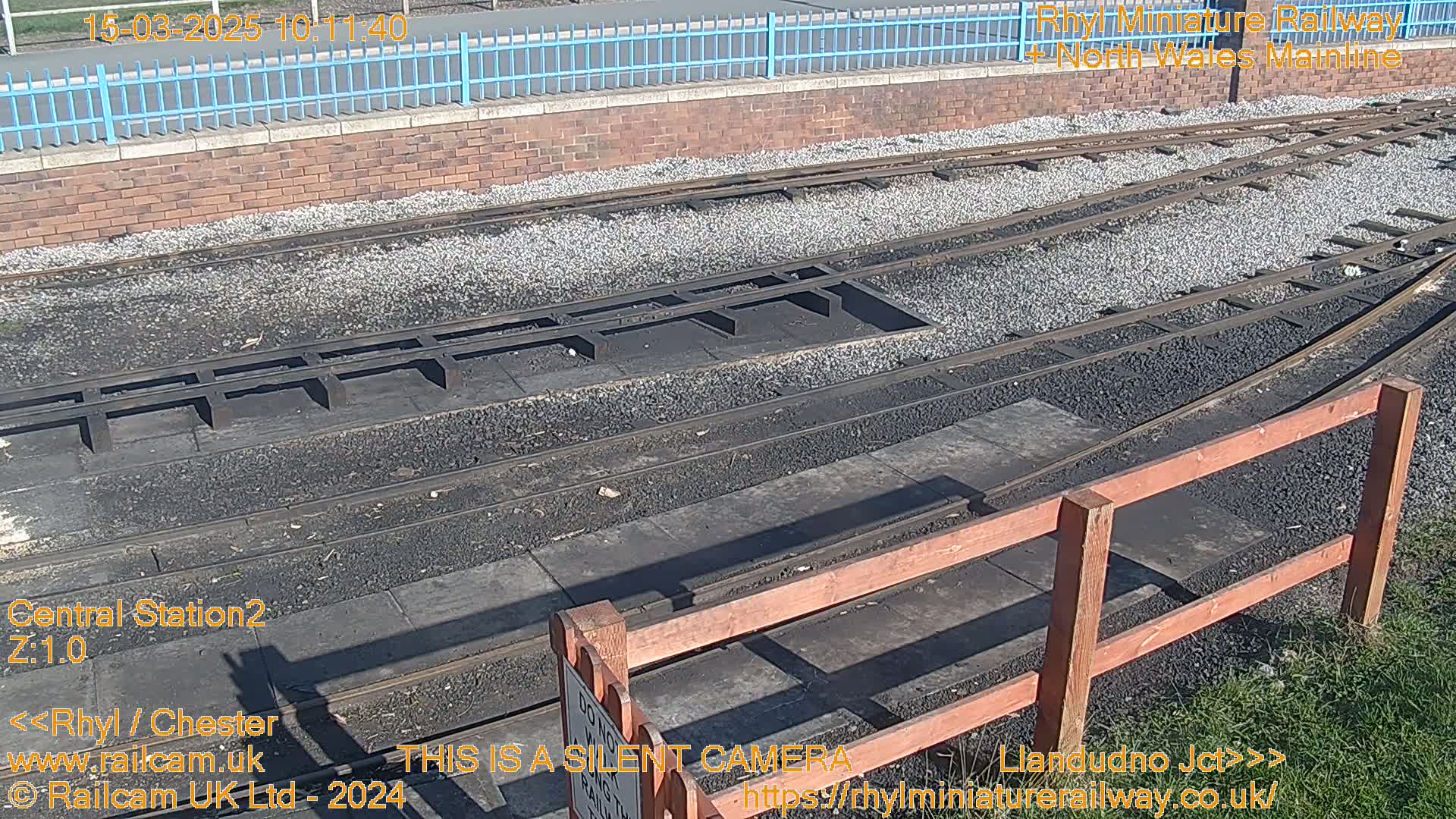 A sunny view of a railway track switching area with a wooden fence and gravel ballast.
