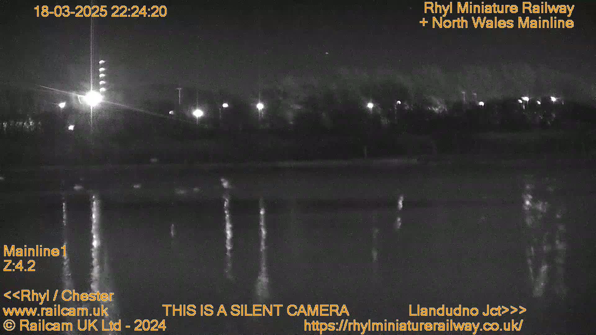 A nighttime view of a dark body of water reflecting lights from a distant roadway and streetlights.
