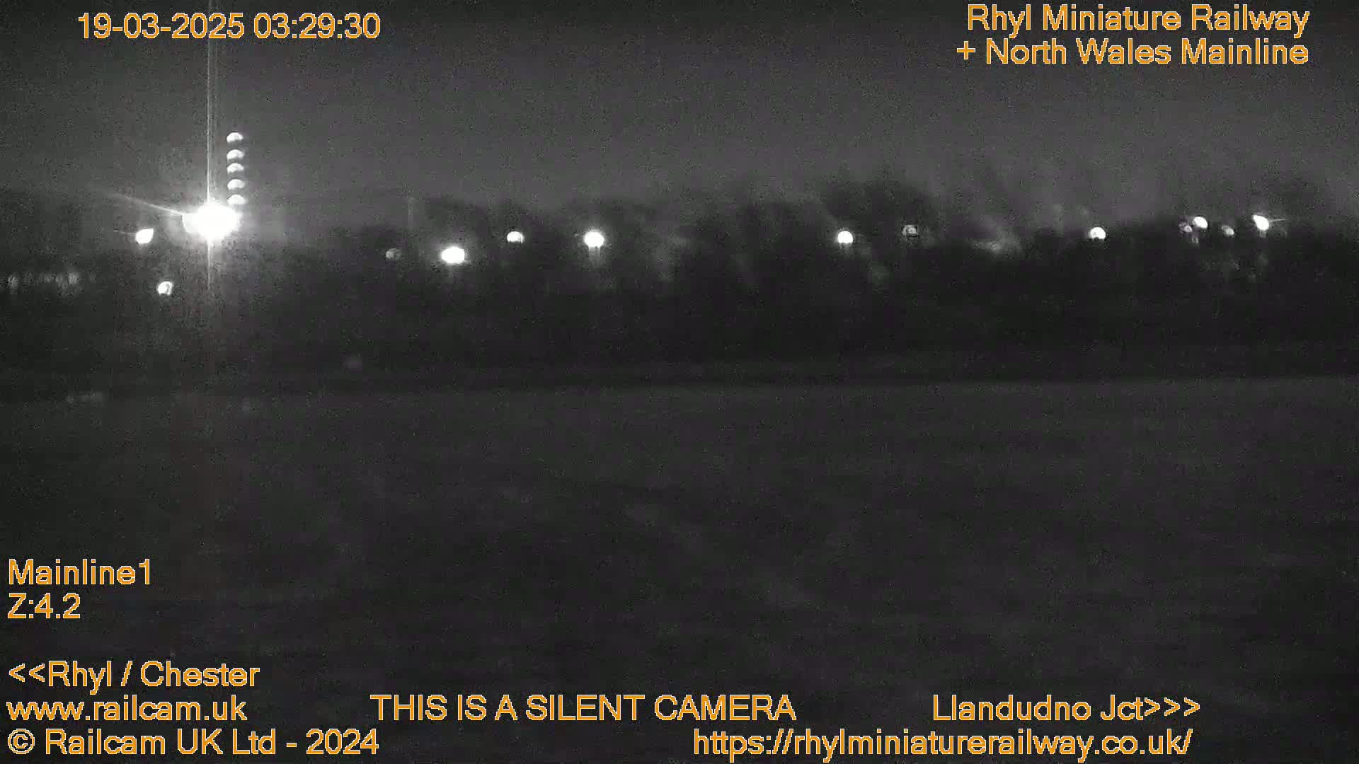 A nighttime, low-light view of a dark landscape with several illuminated lights in the distance.
