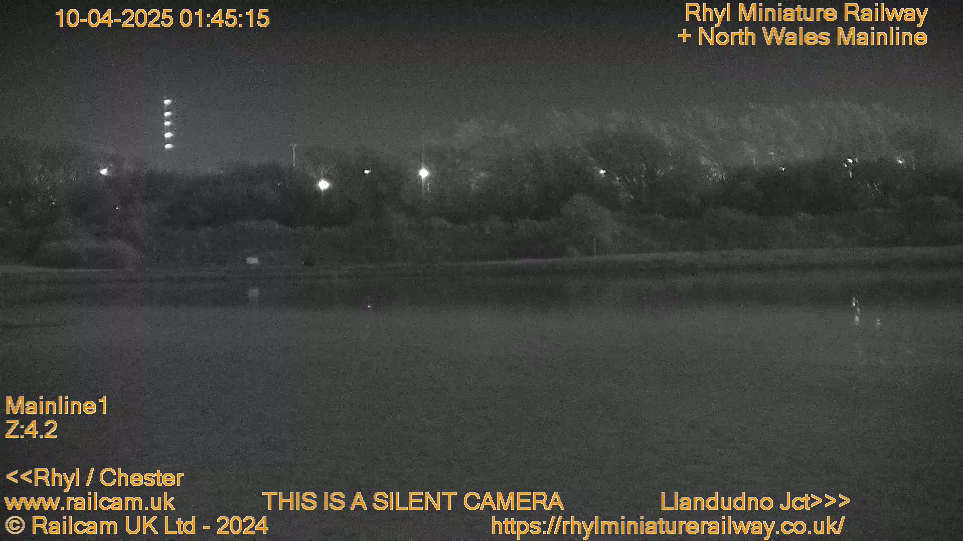 A nighttime, low-light view of a dark body of water bordered by trees and illuminated by distant lights.