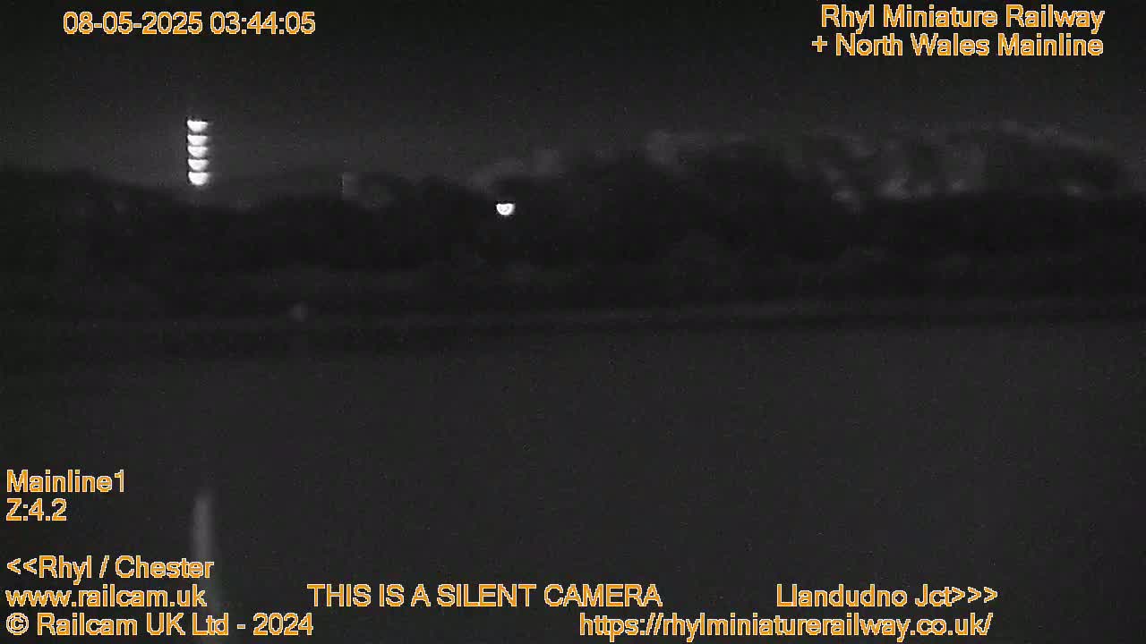 A nighttime, low-light view of a dark landscape with a faintly visible line of lights in the distance.