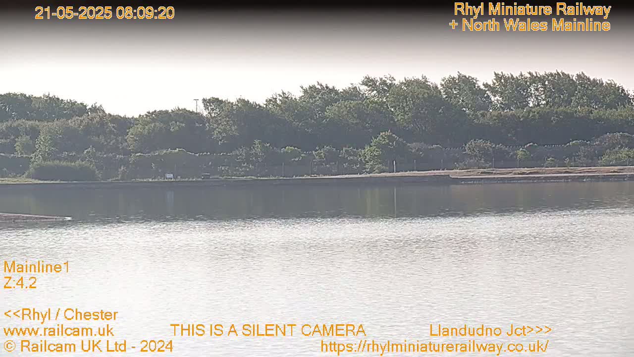 A calm body of water reflects a hazy sky and a line of trees on the far shore.
