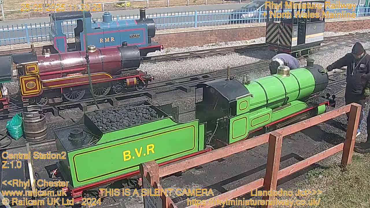 Three small locomotives are parked on railway tracks on a sunny day.