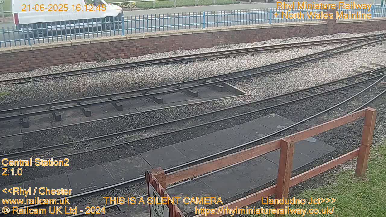 A section of train tracks curves gently, with a white van visible in the background, under overcast skies.