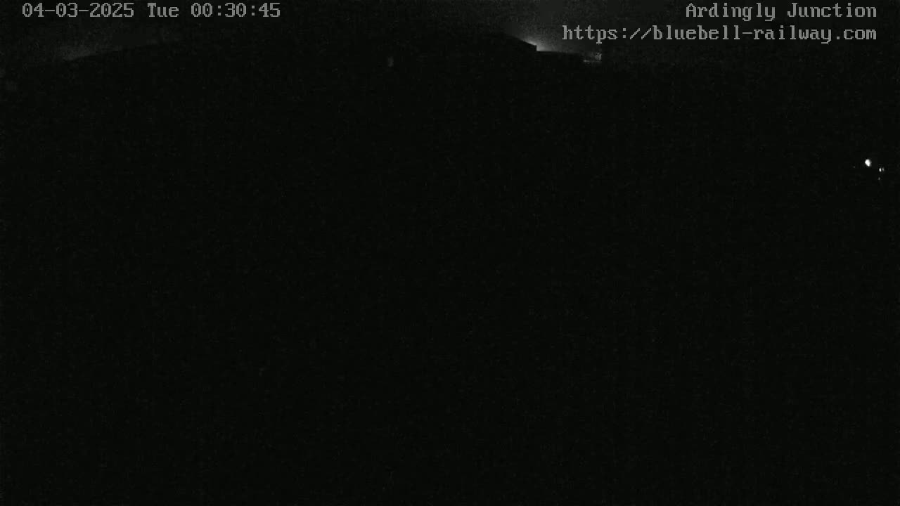 A nighttime, dark image shows a dimly lit structure in the distance under a clear, dark sky.