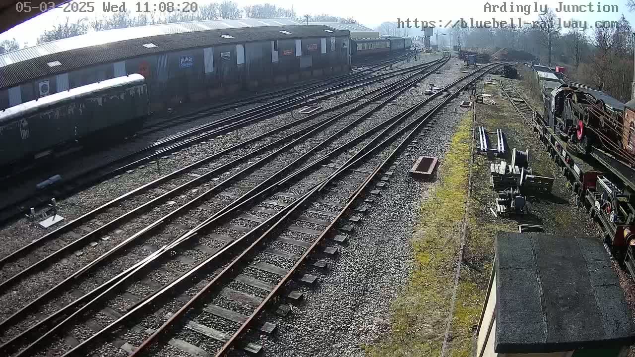 A railway yard with multiple train tracks, railway cars, and a locomotive under a mostly sunny sky.