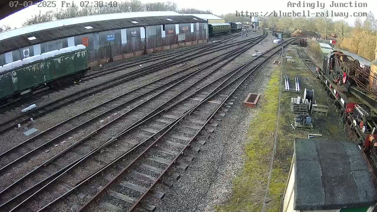 A railway yard with multiple train tracks, a weathered green train car, and several other train cars and locomotives, viewed on a partly sunny day.
