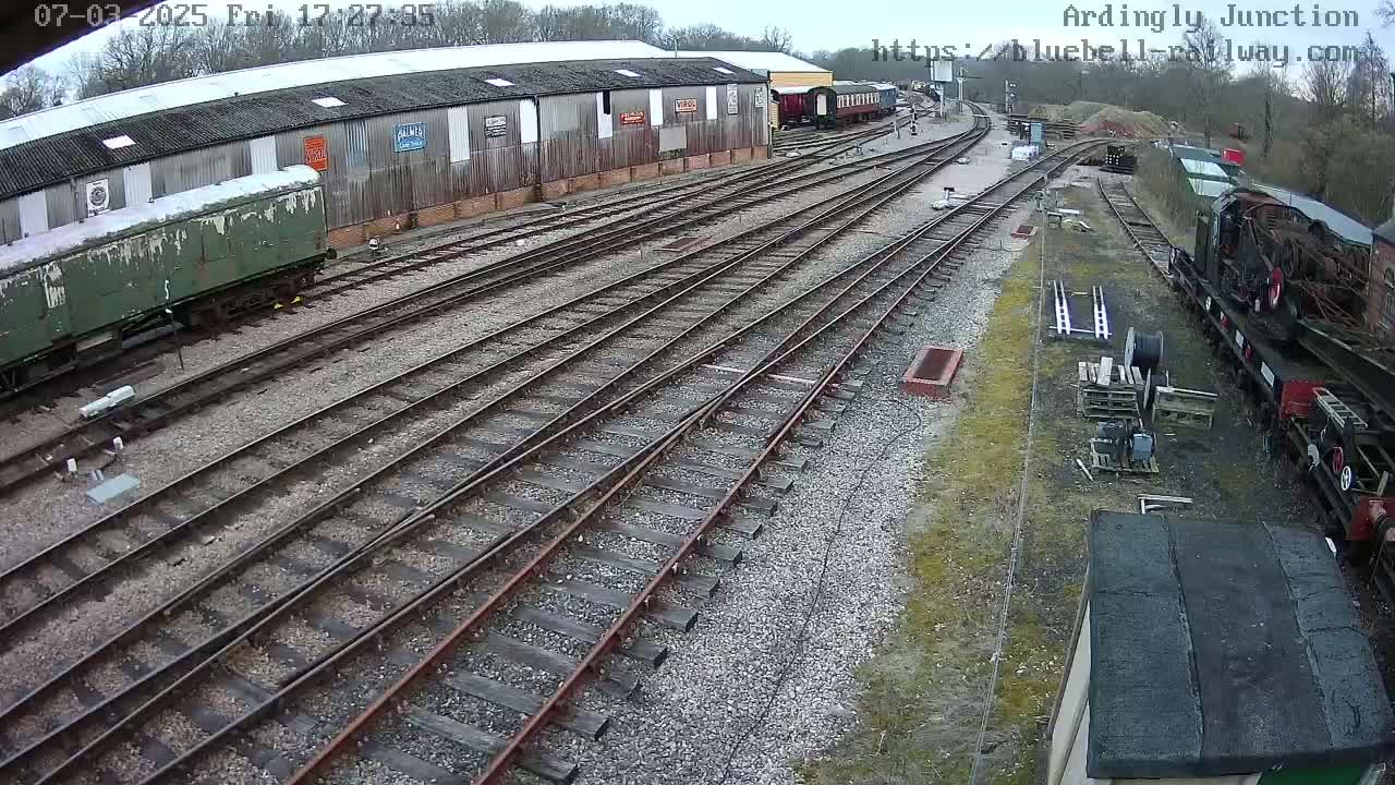 A railway yard with multiple train tracks, railway cars, and a large shed under an overcast sky.