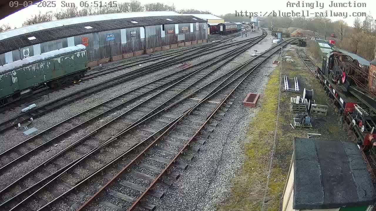 An overcast day reveals a railway yard with multiple train cars, tracks, and a large building.