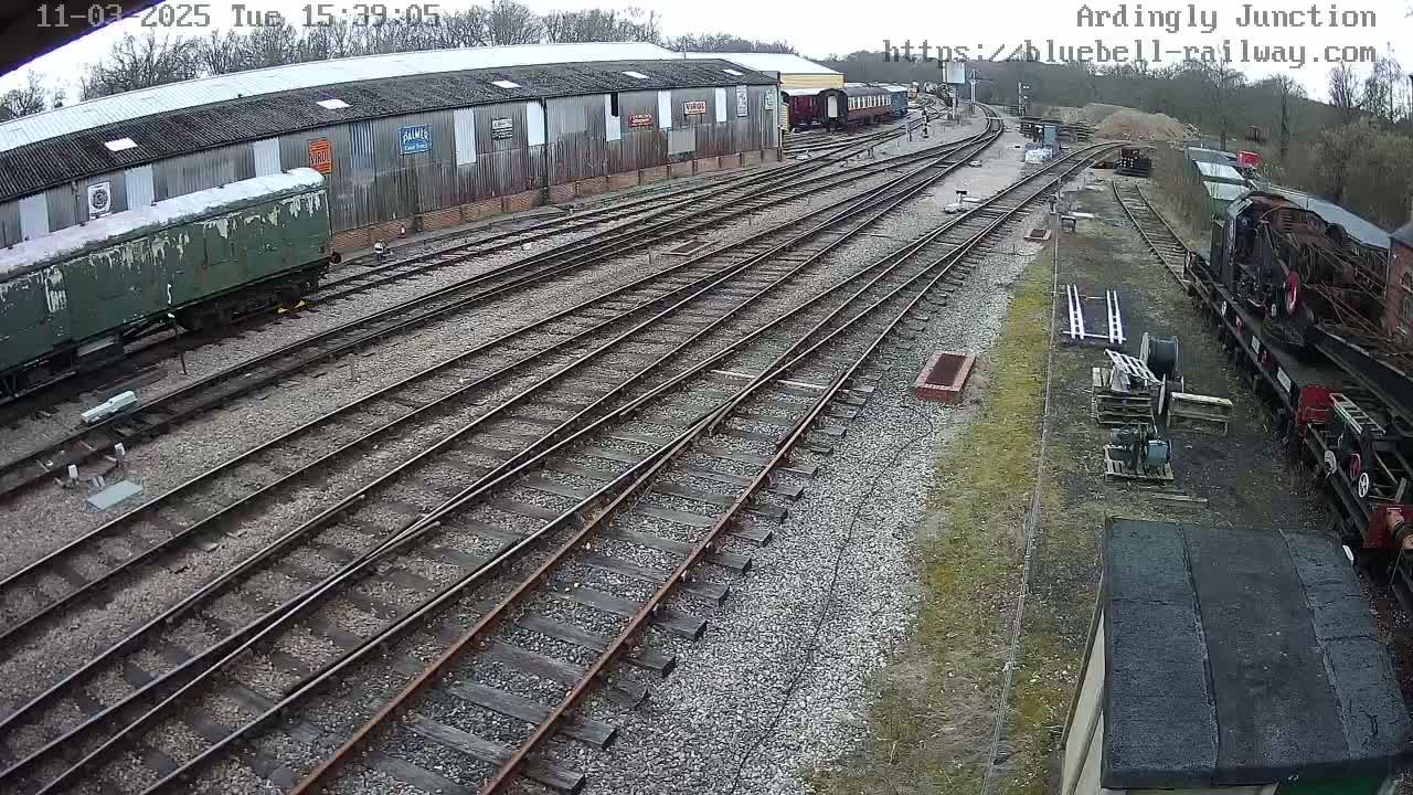 An overhead view of a railway yard on an overcast day shows multiple train cars and tracks branching off from a large building.