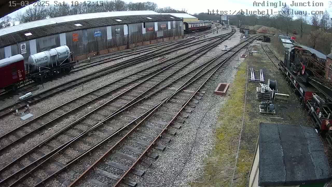 A railway yard with multiple train tracks, railway cars, and a long building under a partly cloudy sky.
