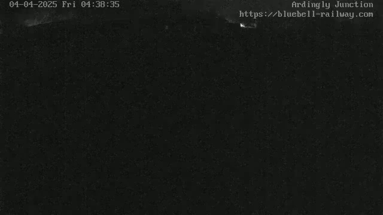 A dark, nighttime image shows a mostly black scene with faint, indistinct shapes in the distance.