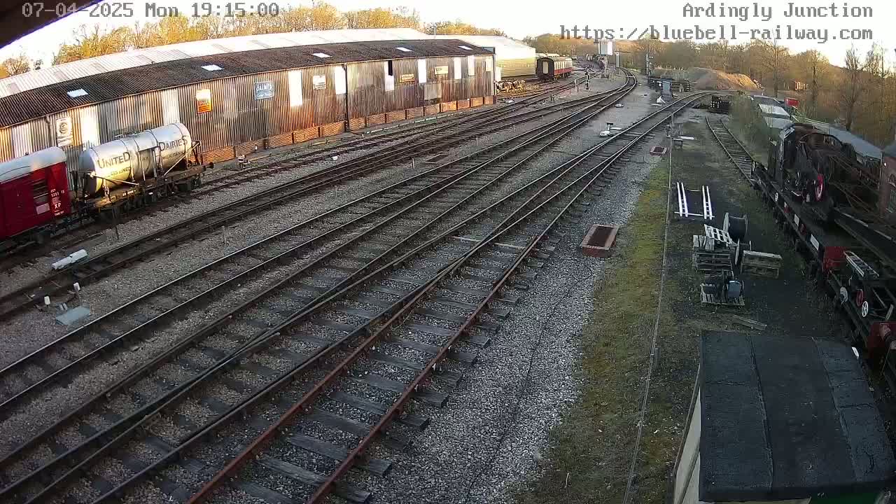 A railway yard with multiple train cars and tracks, under partly sunny evening conditions.
