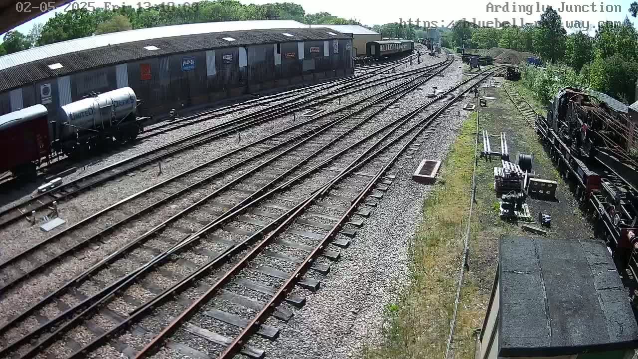 A railway yard with multiple train tracks, several railway cars, and a large building under a sunny sky.