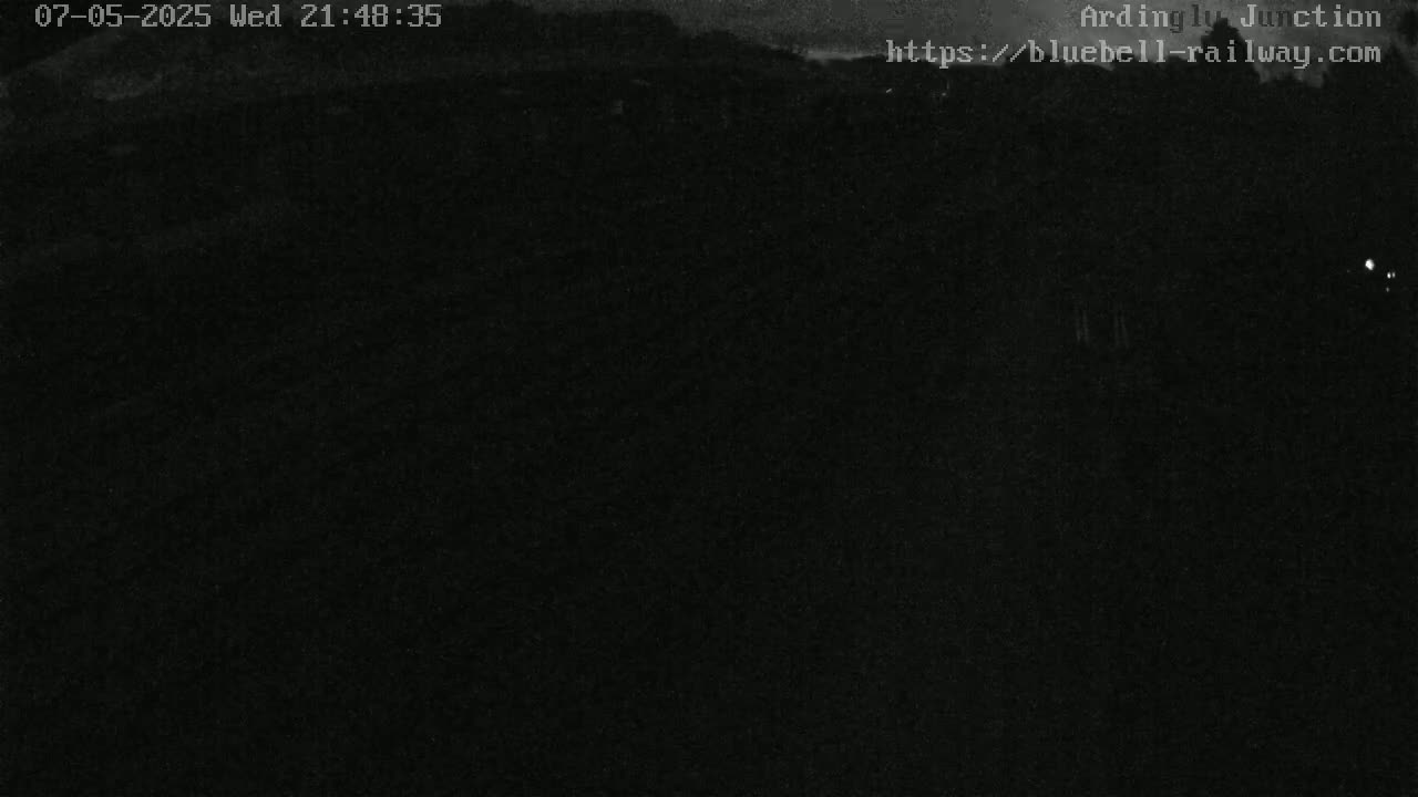 A dark, nighttime view of a landscape, possibly a railway line, under a mostly clear sky.