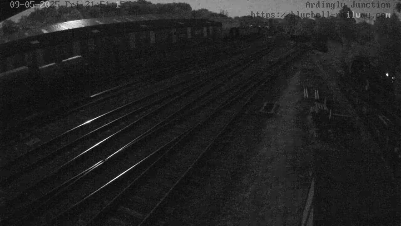A nighttime, low-light view shows multiple sets of train tracks extending into the distance, next to a dark building.