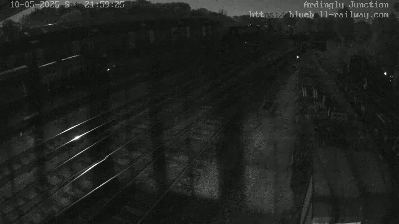 A nighttime, high-angle view of train tracks with dimly lit train cars visible in the distance.