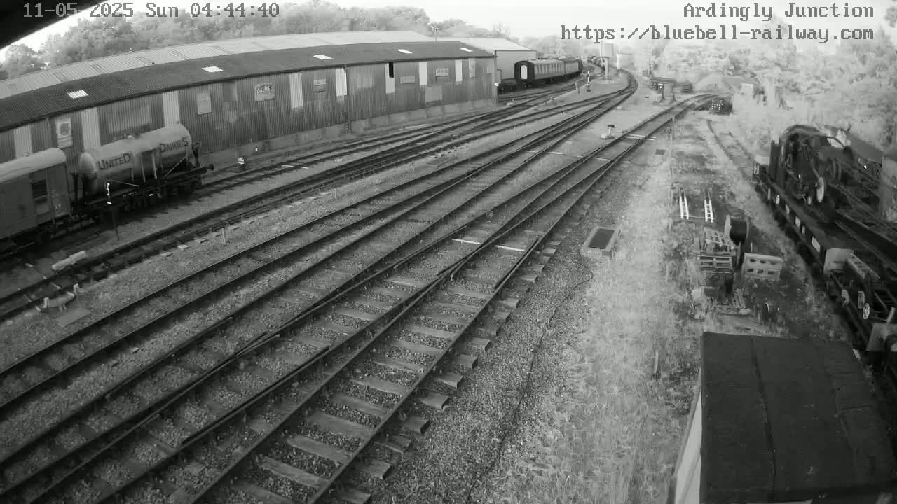 A railway yard with multiple train tracks, several rail cars, and a long building under an overcast sky.