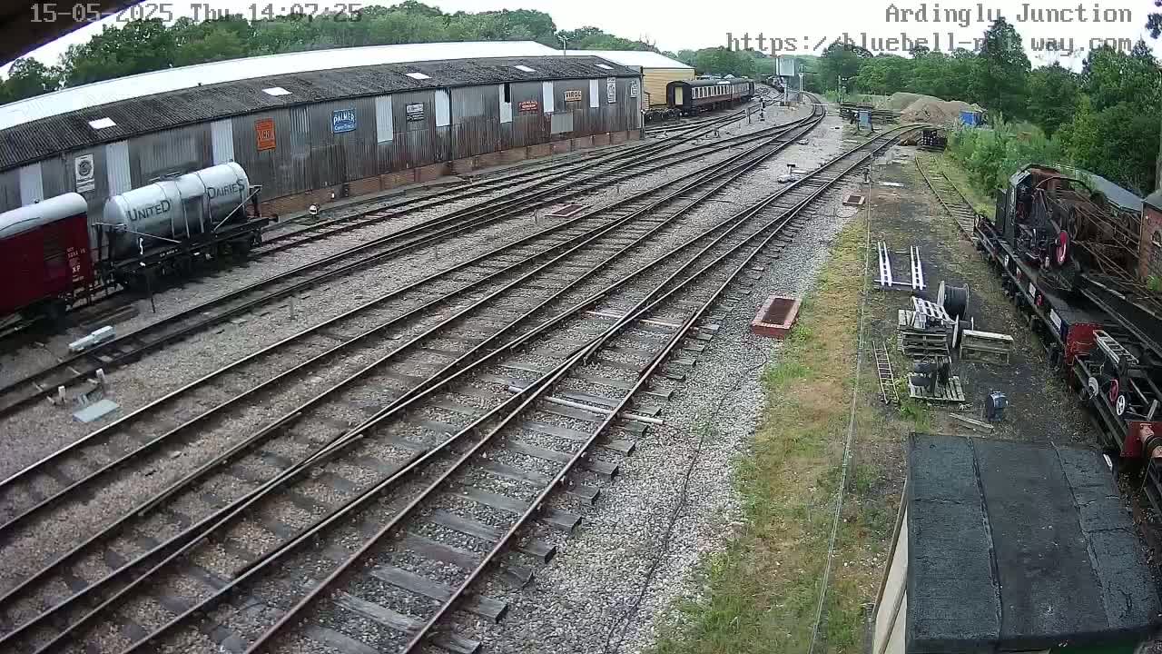 A railway yard with several train cars and a long shed, under a partly sunny sky.