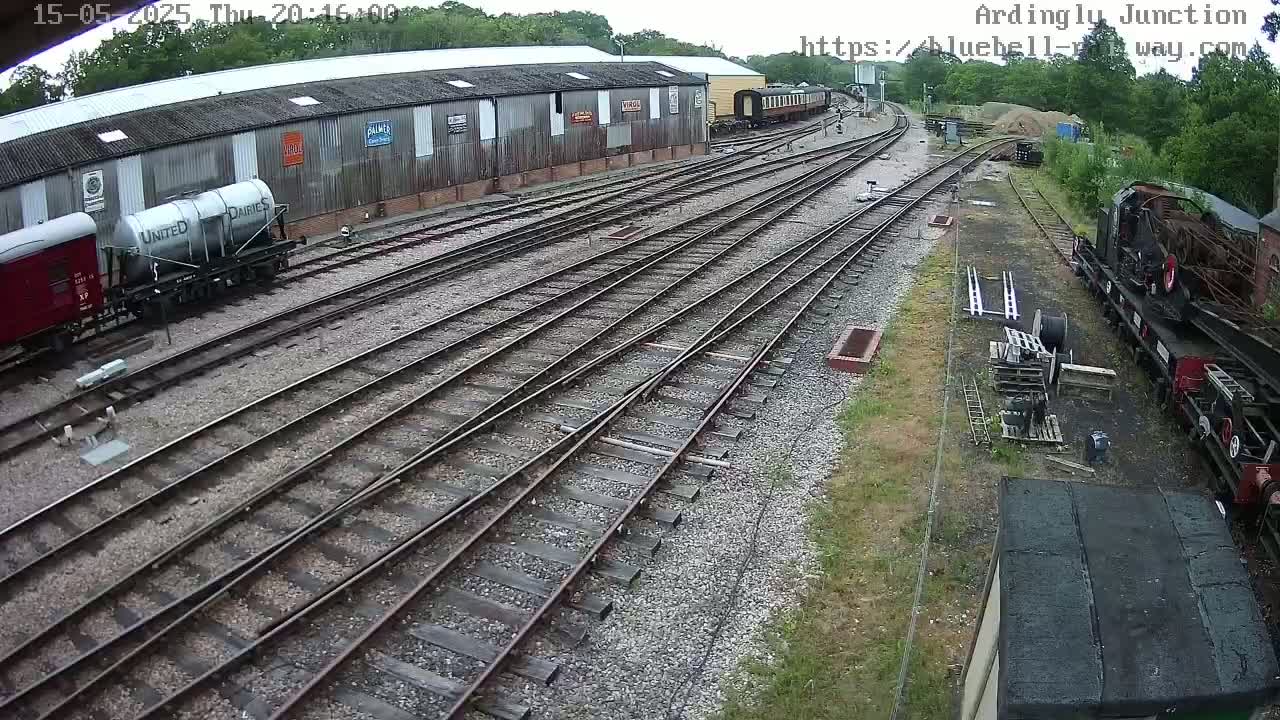 A railway yard with several train cars and locomotives, some parked and others on tracks, under partly cloudy skies.