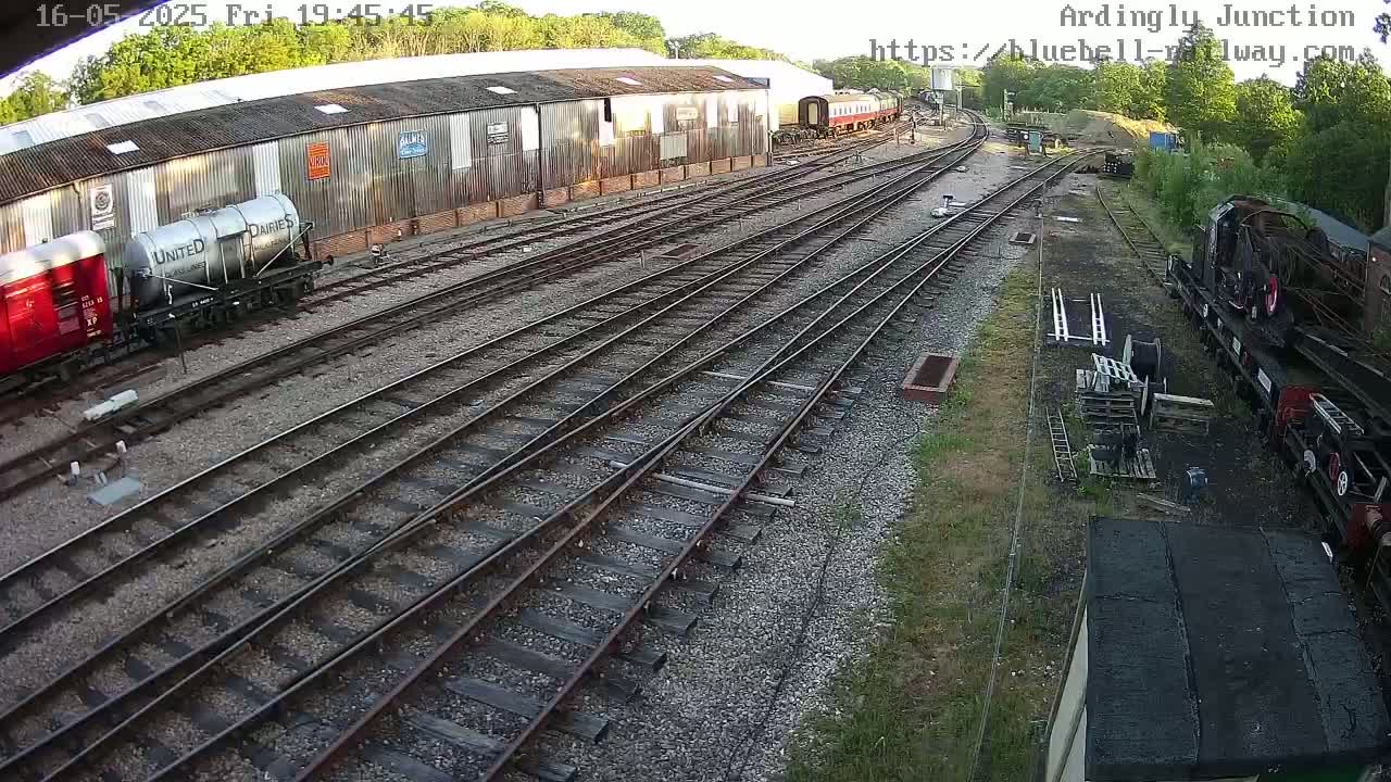 A railway yard with multiple train cars and tracks, some under a large building, in the late afternoon.