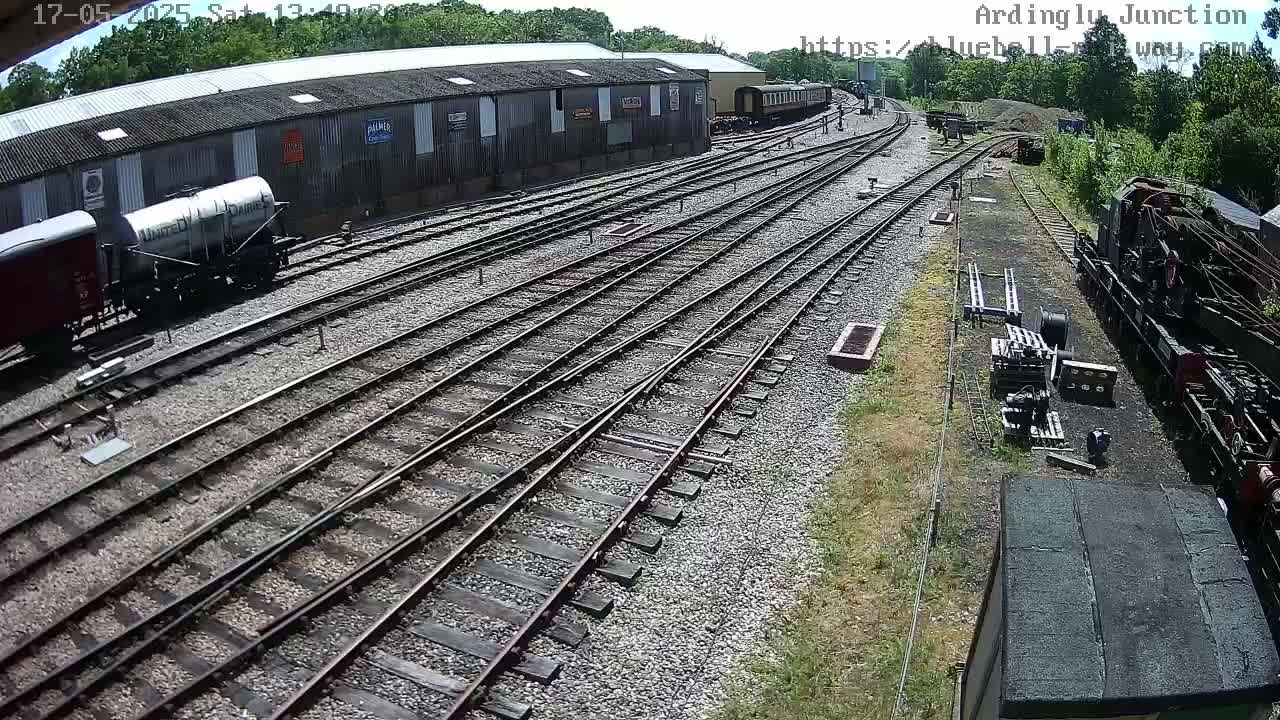 A high-angle view of a railway yard on a sunny day, showing several train cars, railway tracks, and a long shed.