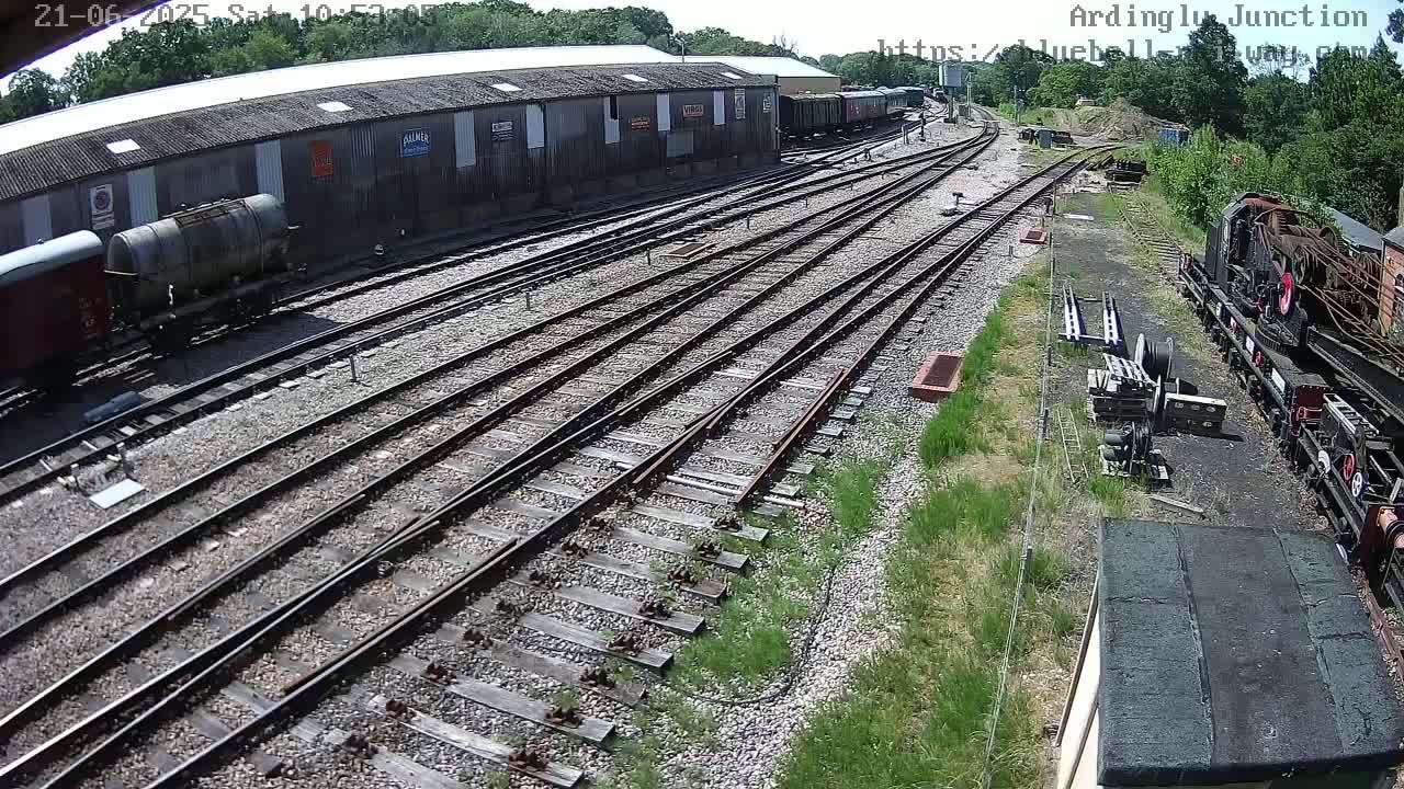 A high-angle view of a railway yard on a sunny day, showing multiple train tracks, railway cars, and a locomotive.