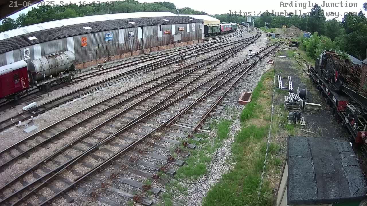 An overcast day at a railway yard shows multiple train tracks branching out from a long building with railway cars and locomotives parked alongside.