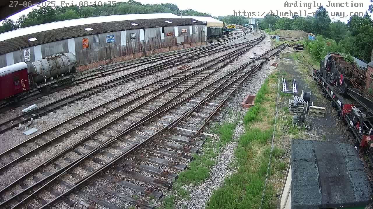 A railway yard with multiple train tracks, railway cars, and a long building, on an overcast day.