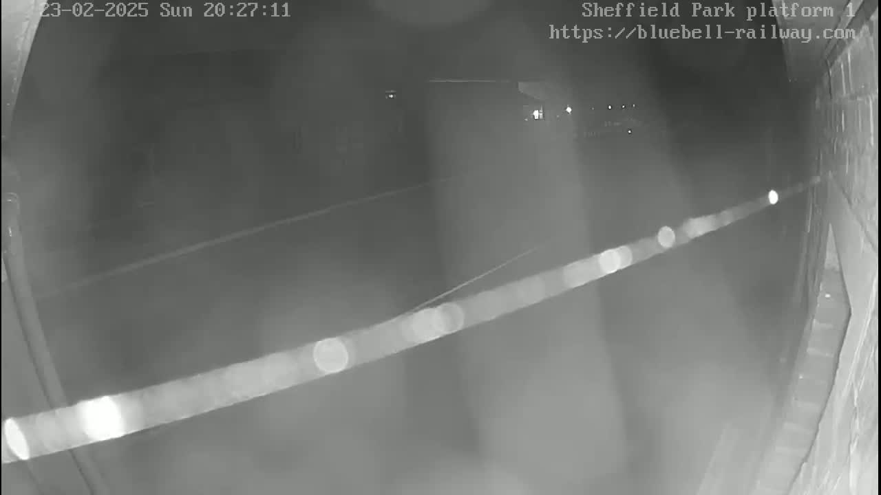 A nighttime, low-light security camera view shows a dark, empty platform area extending into the distance.